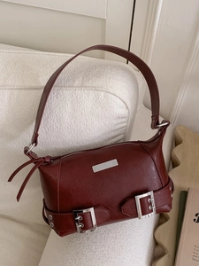 Retro burgundy shoulder bag with silver hardware and tassels on a cream sofa