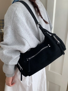 Sac à bandoulière en daim noir minimaliste avec zips argentés porté par un mannequin