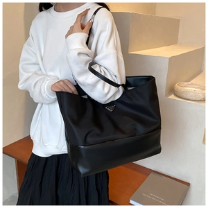 Detail of black oxford tote bag with leather straps and triangular metal logo plate