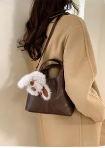 Detail of dark brown leather tote bag with white plush bunny charm on beige wool coat