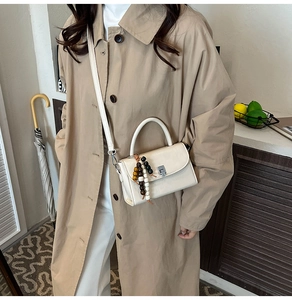 Close-up of cream-white mini handbag featuring a colorful wooden bead charm and metal lock