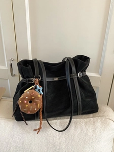 Minimalist black suede tote bag with leather straps and donut charm on a sofa