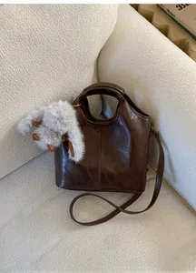 Detail view of coffee brown bucket bag with plush rabbit charm on a cozy white sofa
