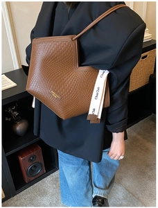 Gros plan du sac cabas tissé marron avec coupe asymétrique et sangle décorative lettrée