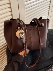 Fashionable dark brown matte leather tote bag with unique knotted handle and plush charm