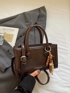 Sac à main rétro en cuir marron foncé avec charme en bois sur un costume gris