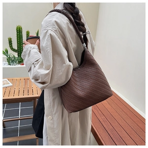 Detailed close-up of dark brown woven texture and twisted shoulder strap of the bucket bag