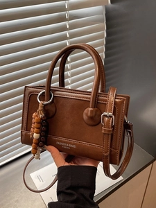 Sac Boston vintage en cuir marron avec poignées et pendentif perlé sous un jeu d'ombres