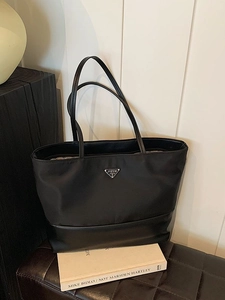 Black Oxford cloth tote bag with metal triangle logo on a dark leather bench