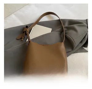 Détail du sac seau en cuir marron avec texture litchi et plaque de logo dorée