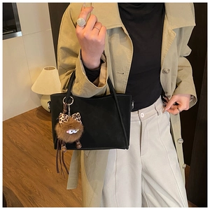 Detail of black suede bucket bag featuring a quirky plush monster charm on the handle