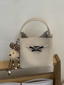 Cream lychee textured bucket bag with puppy charm and metal buckle detail on wooden shelf