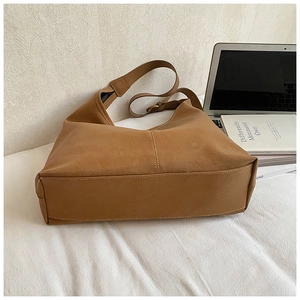 Close-up of retro brown tote bag with soft texture and wide strap on white fabric