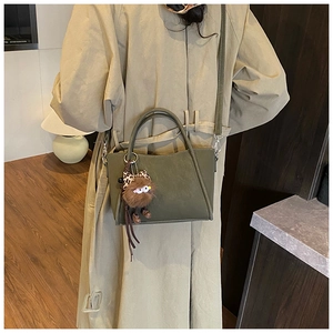 Detail of army green matte suede bucket bag with leopard bow charm on khaki trench coat