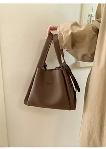 Brown litchi grain leather bucket bag shown held by model against a cream wall