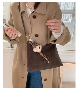 Detail of a dark brown matte leather baguette bag with a cute leopard bow plush bear charm