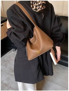 Sac seau en cuir grainé marron avec logo doré porté par un mannequin en blazer noir