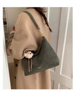 Close-up of green suede baguette bag with gold hardware and a cute teddy bear charm