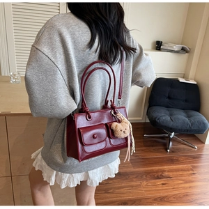 Detail of dark red leather tote bag with functional pockets and plush bear charm