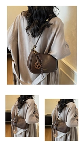 Detail of vintage dark brown faux leather crossbody bag with golden logo and pretzel charm