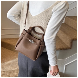 Brown lychee leather bucket bag with metal turn-lock closure worn by a model