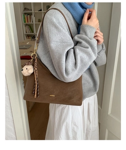 Detail of dark brown tote bag with bear charm and braided tassel in lifestyle scene