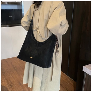Detail of black suede hobo bag with gold metal trim and tassel on a khaki trench coat