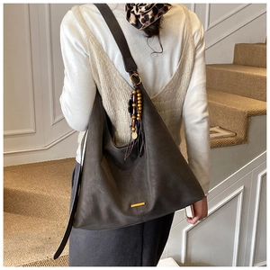 Detail van grijze leren hobo tas met gouden logo plaatje en houten kralen kwastje