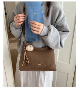 Brown faux suede shoulder bag with golden hardware and fuzzy charm detail on model