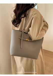 Detail of grey pebbled leather tote bag with gold twist lock on beige trench coat