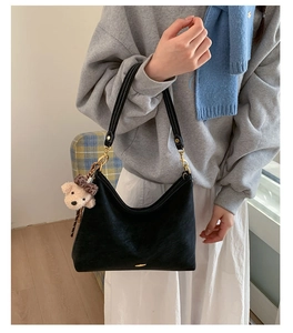 Detail of black leather half-moon baguette bag with golden hardware and teddy bear charm