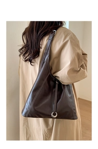 Détail d'un sac hobo en cuir marron foncé avec surpiqûres sur un trench-coat beige