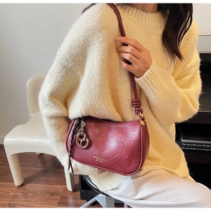 Detail of burgundy leather shoulder bag with decorative knot and golden ring hardware