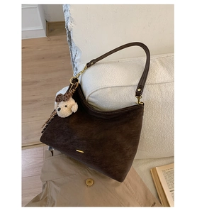 Detail of dark brown suede half-moon bag with gold metal buckle and plush bear charm