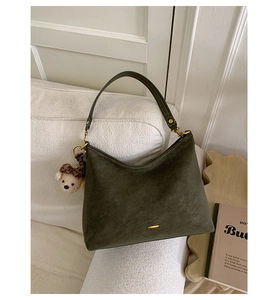 Detailed macro view of olive green suede shoulder bag with gold hardware and bear charm