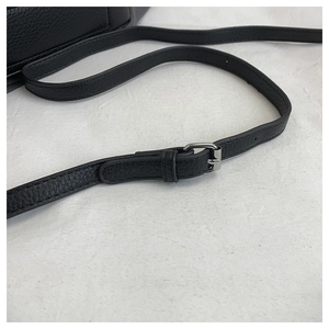 Macro detail of adjustable black pebble grain leather strap with silver buckle on the bag