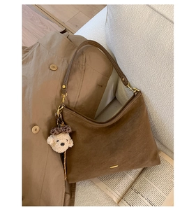 Detailed texture of brown suede shoulder bag with plush bear charm and gold hardware