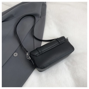 Detail of black lychee grain leather crossbody bag with silver hardware on a blazer