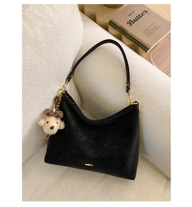 Detail of black suede crescent bag with gold hardware and plush puppy charm accessory