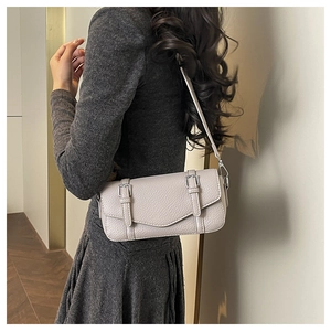 Side view of light grey pebbled leather baguette bag worn over the shoulder by a model