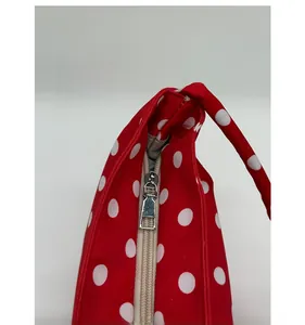 Detail of smooth silver zipper on a red fabric bag with classic white polka dots
