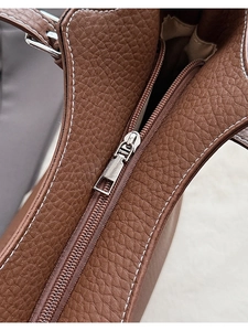 Close-up of brown pebbled leather texture with silver zipper and white contrast stitching