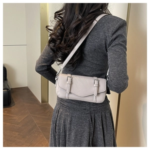 Close-up of a grey litchi grain leather satchel bag with metallic buckles on a model