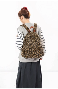 Detail eines Canvas-Rucksacks mit Leopardenmuster, großem Fach und Seitentaschen am Modell