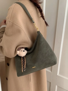 Retro dark green suede shoulder bag with bear charm and gold hardware on camel coat