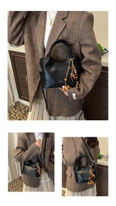 Detail of black bucket bag with wooden bead charm and adjustable crossbody strap