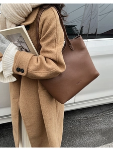 Detail of brown lychee grain leather tote bag with white contrast stitching and gold logo