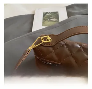 Macro shot of brown quilted leather handbag with gold metal hooks and dual zipper details