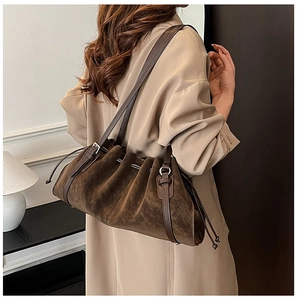 Detailed close-up of brown suede shoulder bag with pleated drawstring design and leather strap