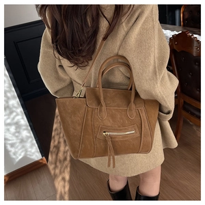 Nahaufnahme der karamellbraunen Retro-Muschel-Tasche mit Quasten-Detail am Modell